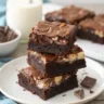 Stack of rich, fudgy Heavenly Hash Brownies with marshmallow and nut filling, served on a white plate with chocolate chunks and a glass of milk.