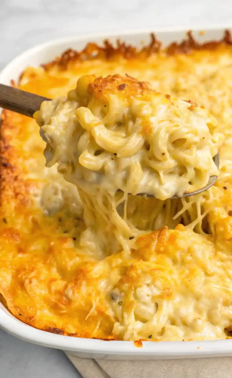 A close-up of creamy, golden-baked Tini’s Mac and Cheese being scooped from a casserole dish, with melted cheese stretching from the spoon.