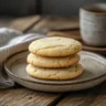 Soft and chewy sugar cookies stacked on a ceramic plate with tea on a rustic wooden table