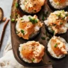 Baked sushi bites in a muffin tin, featuring rice and spicy salmon topped with creamy orange sauce, green onions, and sesame seeds.