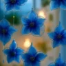 Hanging blue flower-shaped suncatchers made of translucent fabric or plastic, each with a beaded center, strung on clear lines in front of a softly lit background.