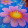Colorful salt painting of a purple flower with orange and yellow center, with a dropper applying watercolor.
