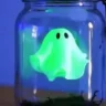 Glowing green ghost in a jar Halloween craft with black eyes, floating above moss inside a mason jar.