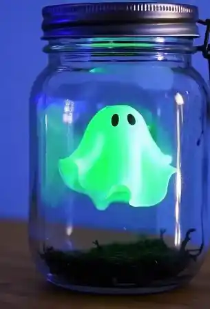 Ghost in a Jar: A Cozy Halloween Craft with Heart 3 Glowing green ghost in a jar Halloween craft with black eyes, floating above moss inside a mason jar.