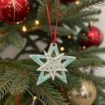 Handmade Double Star Ceramic Christmas Ornament hanging on a Christmas tree with red ribbon and holiday lights.