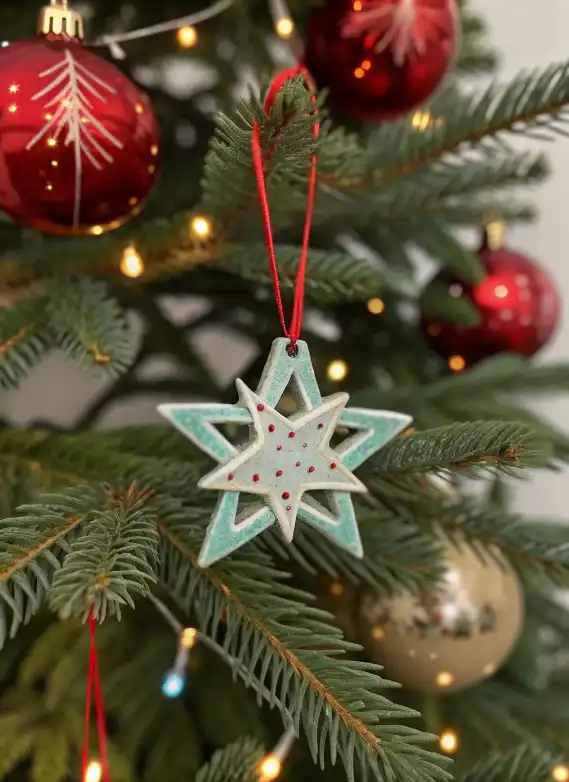 Handmade Double Star Ceramic Christmas Ornament hanging on a Christmas tree with red ribbon and holiday lights.
