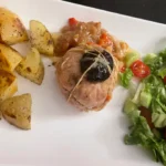 A plated meal featuring a veal paupiette topped with a prune, served with roasted potatoes, sweet potatoes, and a fresh salad of lettuce, cherry tomatoes, and cucumber.