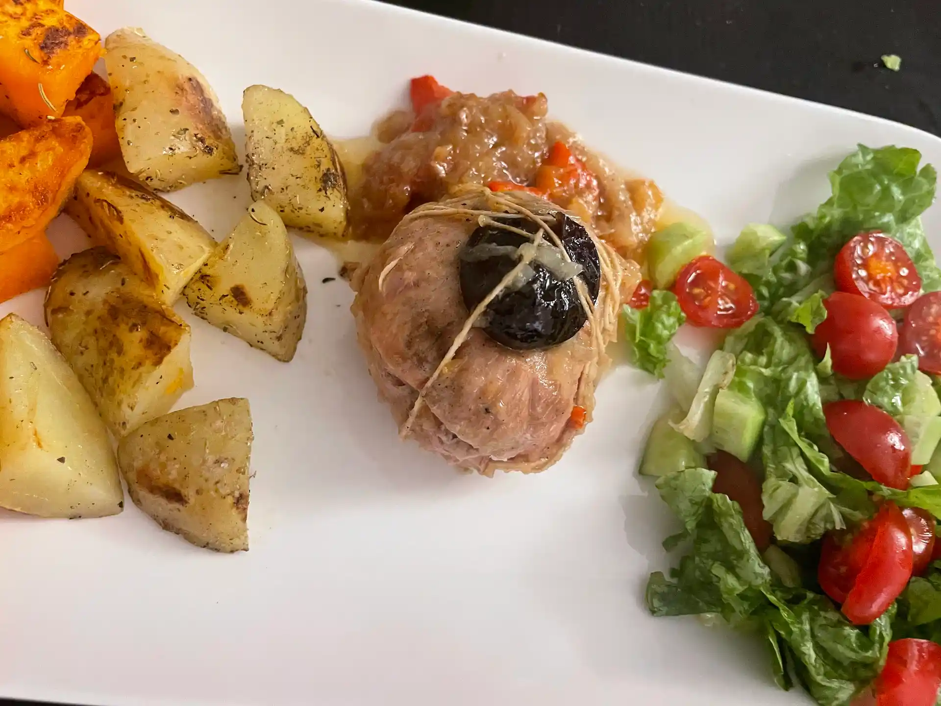 Veal Paupiettes: A Tender French Classic with a Sweet Surprise 4 A plated meal featuring a veal paupiette topped with a prune, served with roasted potatoes, sweet potatoes, and a fresh salad of lettuce, cherry tomatoes, and cucumber.