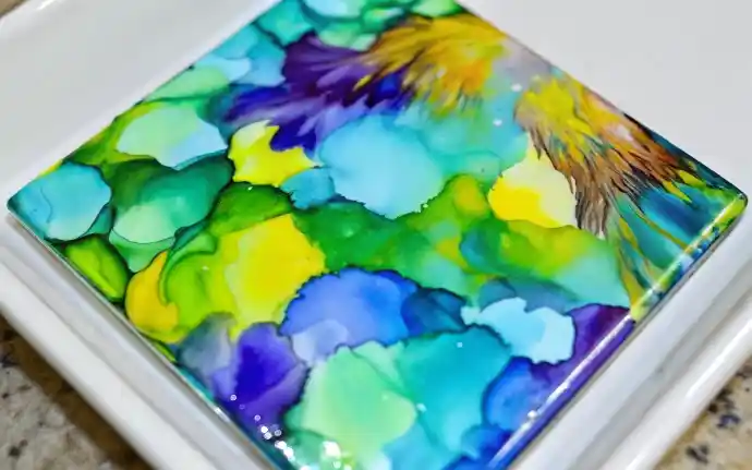 How to Paint With Sharpies and Alcohol: A Beautiful, Budget-Friendly DIY Anyone Can Do 4 Abstract alcohol ink art on a ceramic tile with vibrant blues, greens, yellows, and purples.